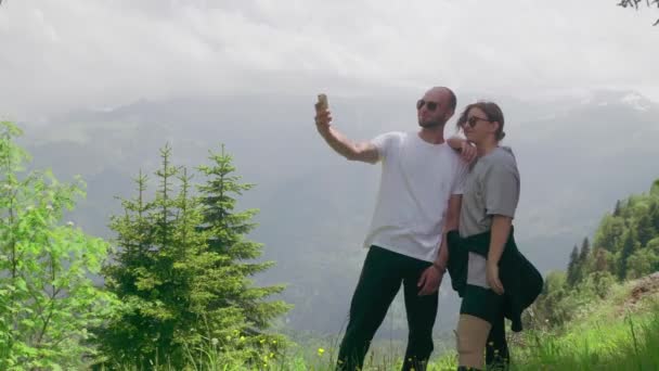 Ένας νεαρός άνδρας και ένα κορίτσι στέκονται σε μια ορεινή περιοχή και βγάζουν selfie στο τηλέφωνό τους. Ταξίδι — Αρχείο Βίντεο