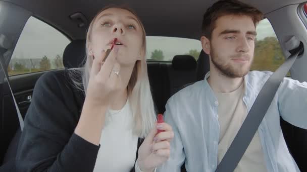A guy and a girl are driving a car. The guy slows down sharply, and the girl, putting on lipstick, accidentally smears her makeup. People are driving in a car — Stock Video