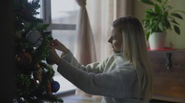 Süveter giyen genç ve güzel bir sarışın Noel ağacının yanında oturuyor ve bir Noel balosu düzenliyor. Evin penceresinin yanında altında hediyeler olan bir Noel ağacı..