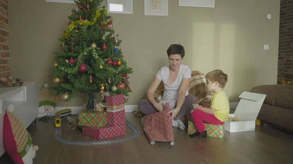 En mor och ett barn packar en gåva i ett vackert omslagspapper. Julen. Feststämning. — Stockfoto