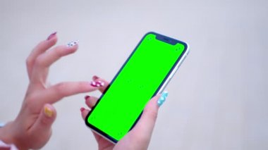 Evinde yeşil ekranlı cep telefonu tutan bir kadının yakın çekimi. Kromakey anahtarlı akıllı telefon teknolojisi üst görüşlü, cep telefonunu elle tutma konsepti.