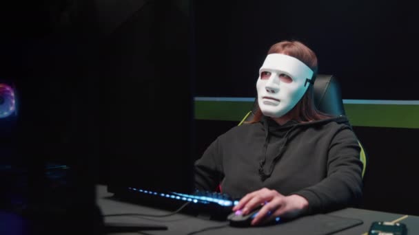 Хакерка за комп'ютером знімає маску з обличчя і дивиться на камеру — стокове відео
