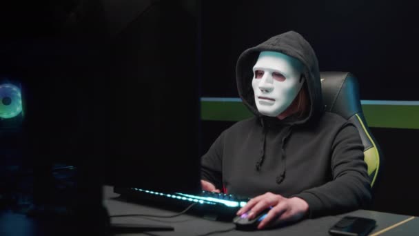 The hacker girl at the computer removes the mask from her face and looks at the camera — Stock Video