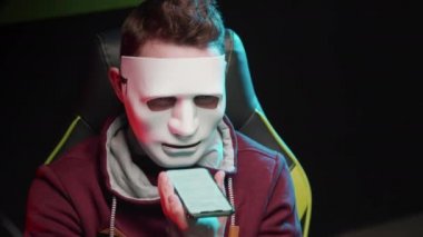 Maskeli bir adam oturuyor ve yakın plan bir telefondan mesaj okuyor.