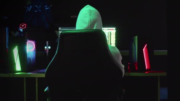 Πορτρέτο ενός μυστηριώδους χάκερ σε μια κουκούλα, κάθεται σε ένα τραπέζι και κοιτάζοντας την κάμερα μετά hacking μια βάση δεδομένων σε ένα σκοτεινό δωμάτιο με κινούμενα σχέδια των κωδικών του συστήματος στο παρασκήνιο. — Αρχείο Βίντεο