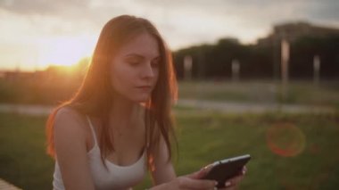 Gün batımında parkta bir kız e-kitap okuyor.