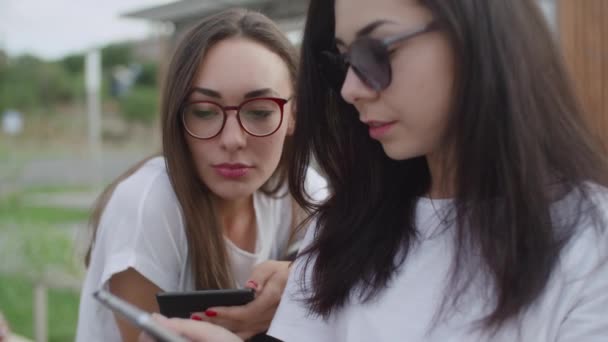 Dos chicas al aire libre leen un libro electrónico — Vídeos de Stock