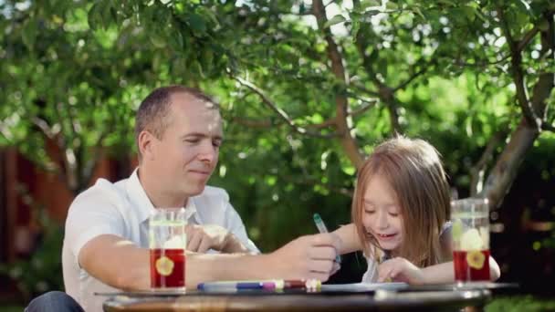 Muž kreslí s dívkou u stolu venku, v létě za teplého slunečného dne — Stock video
