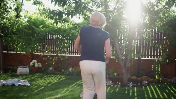 Een oudere vrouw houdt de handen vast van een klein meisje en cirkelt om zich heen, in de zomer buiten — Stockvideo