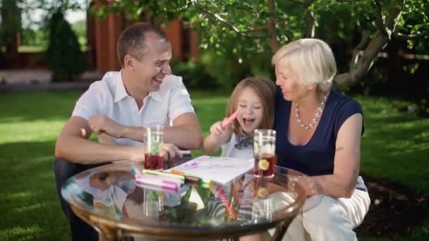 Una famiglia composta da nonna, padre e figlia, attira l'estate a tavola in una calda giornata di sole. — Video Stock