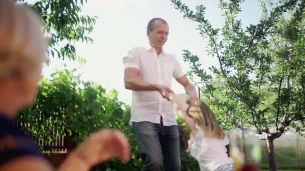A man holds a little girl by the hands and circles around himself outdoors in summer — Stock Video