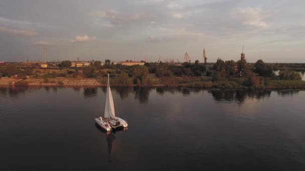 Küçük bir yelkenli yat gün batımında nehirde yelken açar. — Stok video