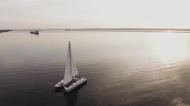 Malá plachetnice pluje po řece při západu slunce