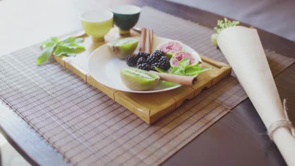 Вкусное фруктовое блюдо на тарелке с ароматным зеленым чаем на деревянном подносе — стоковое видео