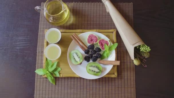 Délicieux plat de fruits sur une assiette avec thé vert parfumé sur un plateau en bois — Video