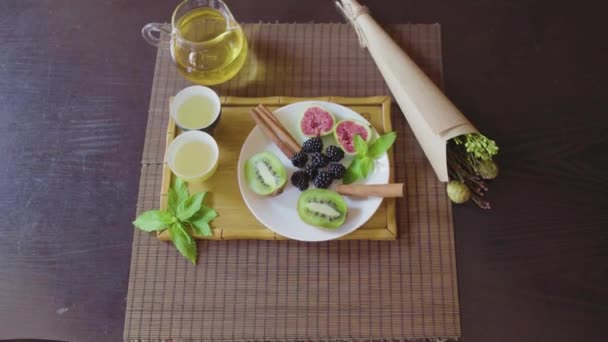 Delicioso plato de frutas en un plato con té verde fragante en una bandeja de madera — Vídeos de Stock