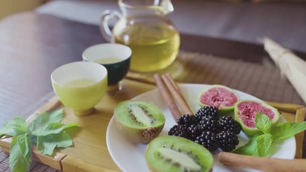 Delicioso plato de frutas en un plato con té verde fragante en una bandeja de madera — Vídeo de stock