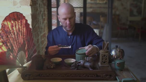 Un joven en una tienda de té pone hojas de té en una cuchara de madera con una espátula de madera — Vídeo de stock