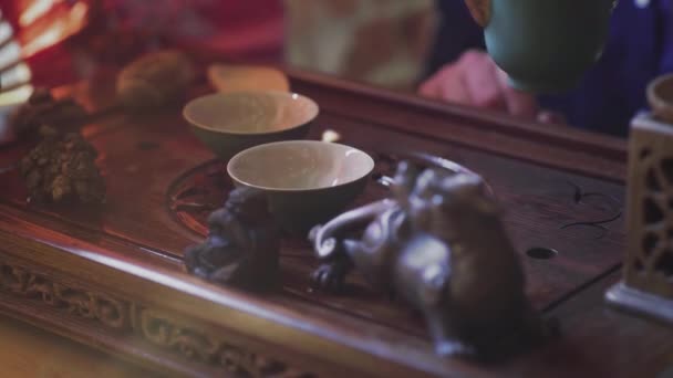 Een man giet thee in theekopjes op een houten dienblad in een theekamer — Stockvideo