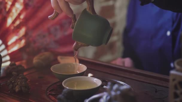 Ένας άνθρωπος ρίχνει τσάι σε φλιτζάνια τσαγιού σε ένα ξύλινο δίσκο σε μια αίθουσα τσαγιού — Αρχείο Βίντεο