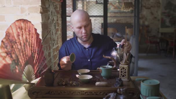 Een man giet kokend water uit een theepot in een theepot voor thee brouwen in een theekamer — Stockvideo