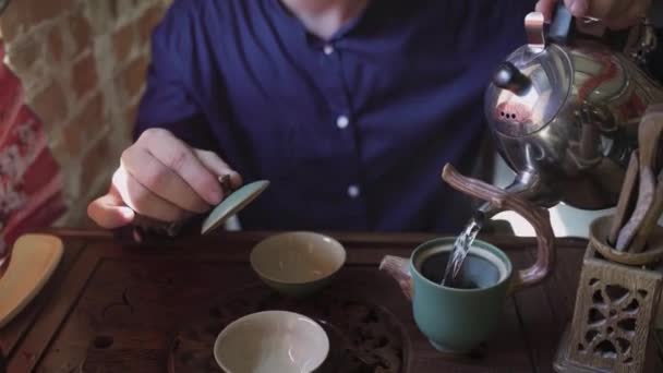 Un hombre vierte agua hirviendo de una tetera en una tetera para preparar té en una sala de té — Vídeo de stock