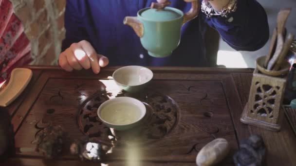 Un hombre vierte té en tazas de té en una bandeja de madera en una sala de té — Vídeo de stock