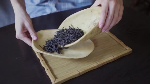 Τα χέρια των γυναικών μεταφέρουν φύλλα τσαγιού από ένα ξύλινο μπολ σε ένα ξύλινο πιάτο στην αίθουσα τσαγιού στο τραπέζι — Αρχείο Βίντεο