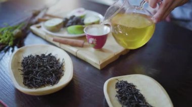 Bir kadının eli masanın üzerindeki çay fincanına yeşil çay döker.