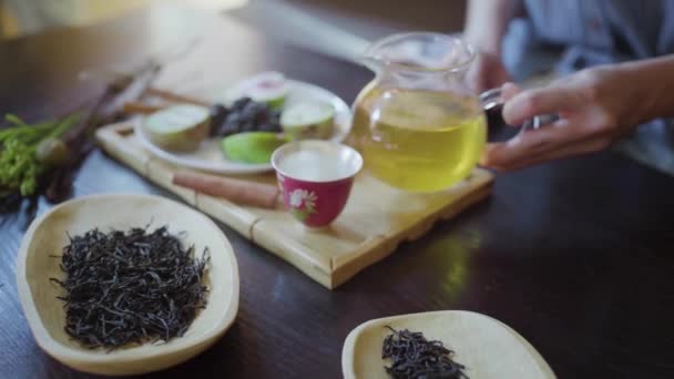 O mână de femeie toarnă ceai verde într-o ceașcă de ceai pe masă — Videoclip de stoc