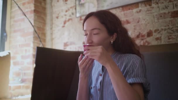 Ένα όμορφο σγουρομάλλικο κορίτσι δοκιμάζει τσάι και απολαμβάνει τη γεύση — Αρχείο Βίντεο
