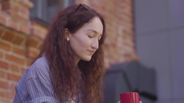 Een mooi krullend meisje drinkt thee en geniet van haar smaak op straat — Stockvideo