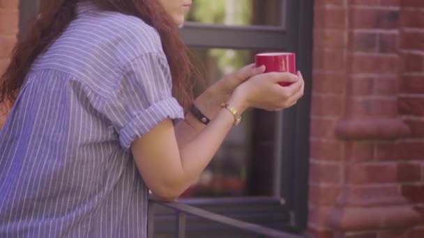 O fată frumoasă cu părul creț bea ceai și se bucură de gustul său pe stradă — Videoclip de stoc