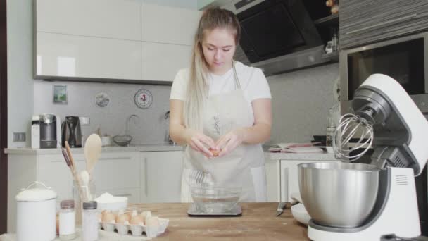 Vacker flicka i köket bryter ett ägg i en glasskål — Stockvideo