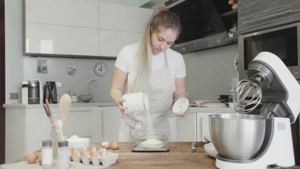 Una chica en la cocina vierte harina en un tazón de vidrio — Vídeos de Stock