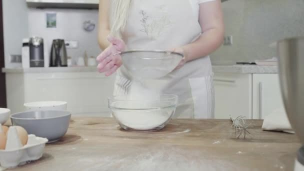 Uma menina na cozinha derrama farinha em uma tigela de vidro — Vídeo de Stock