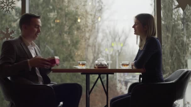 Un hombre y una mujer se sientan uno frente al otro en un café o restaurante junto a la ventana y se comunican. Una cita en un café o restaurante. Ambiente romántico — Vídeo de stock