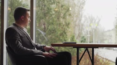 Restoran masasında oturan bir adam saatine bakar, masaya telefonu koyar ve kalkar.