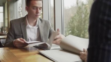 Bir erkek ve bir kadın menüden bir yemek seçiyorlar, pencerenin yanındaki bir kafede karşılıklı oturuyorlar. Hoş bir çiftin randevusu var..