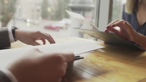 Een man en een vrouw kiezen een gerecht uit het menu, tegenover elkaar zittend aan een tafel in een café bij het raam. Een leuk stel heeft een date. Sluiten. — Stockvideo