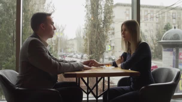 Een man en een vrouw zitten tegenover elkaar in een café of restaurant bij het raam en communiceren. Een afspraakje in een café of restaurant. Romantische sfeer — Stockvideo