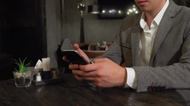 Bir adam bir kafede masada oturuyor, internette web sayfalarını karıştırıyor, bir kadın arkadan yaklaşıyor ve ellerini onun masasına koyup gözlerini kapatıyor.