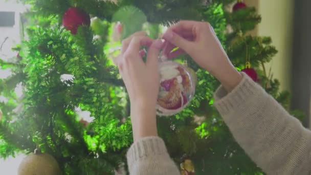 Kobiece dłonie wieszają świąteczną piłkę na choince. Zbliżenie. Święta. Nowy Rok. — Wideo stockowe