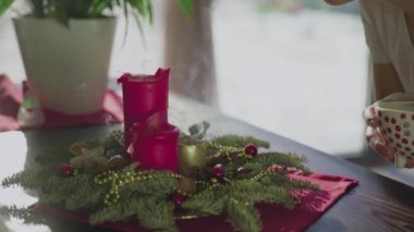 Tanınmayan bir kız, iki kırmızı mum ve bir altın mumla her daim yeşil bir çelenk üflüyor. Noel arifesinde Hıristiyanların gelenek ve adetleri. Bayramın sembolü..