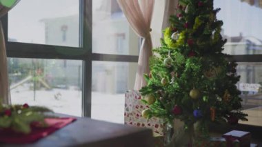 İki kırmızı mum ve bir altın mumu olan ebedi yeşil bir çelenk. Arka planda süslü bir Noel ağacı var. Noel arifesinde Hıristiyanların gelenek ve adetleri.