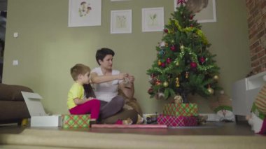 Bir anne ve çocuk güzel bir paket kağıdına hediye koyar. Noel zamanı. Şenlik havası.