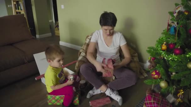 Eine Mutter und ein Kind packen ein Geschenk in ein schönes Geschenkpapier. Weihnachten. Festliche Stimmung. — Stockvideo