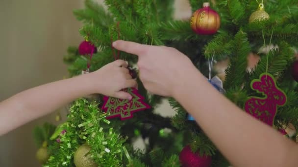 Las manos de una mujer y un niño irreconocibles cuelgan decoraciones en el árbol de Navidad. Humor festivo. — Vídeos de Stock