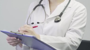 Bir doktorun, boynunda steteskop olan, elinde tablet tutan ve not alan tıbbi önlüklü bir kadının fotoğrafını çek.
