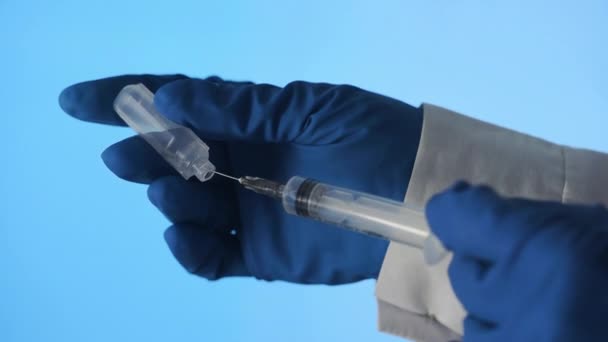 Gros plan des mains d'un médecin préparant un vaccin injectable sur fond bleu — Video